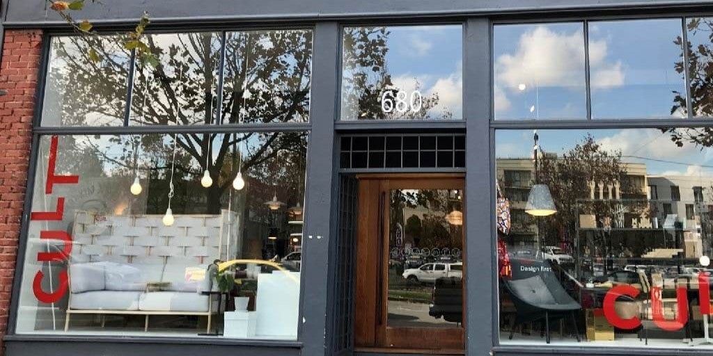 Storefront with large windows displaying interior decor and street view.