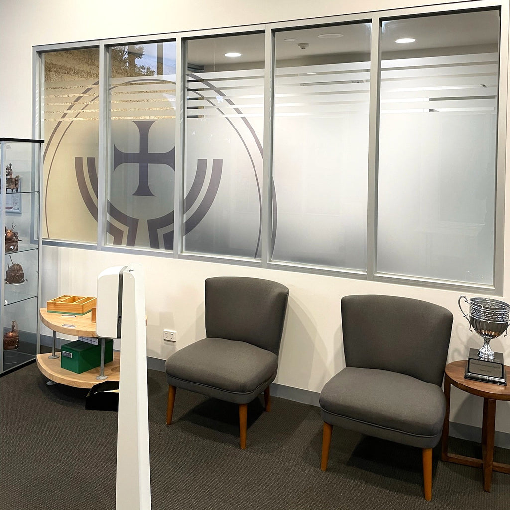 Two gray chairs in a room with a decorative window film and small tables.